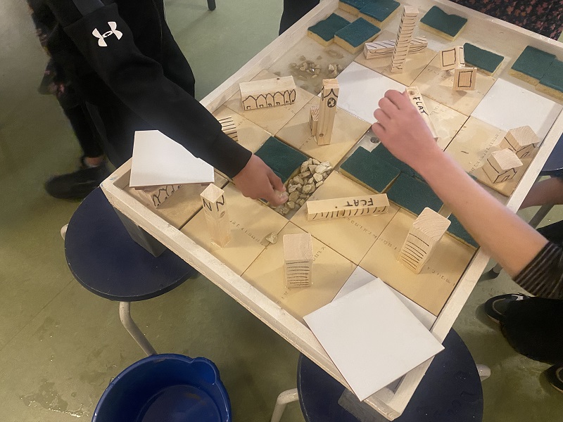 kinderhanden zetten houten modellen van gebouwen op een speelbord
